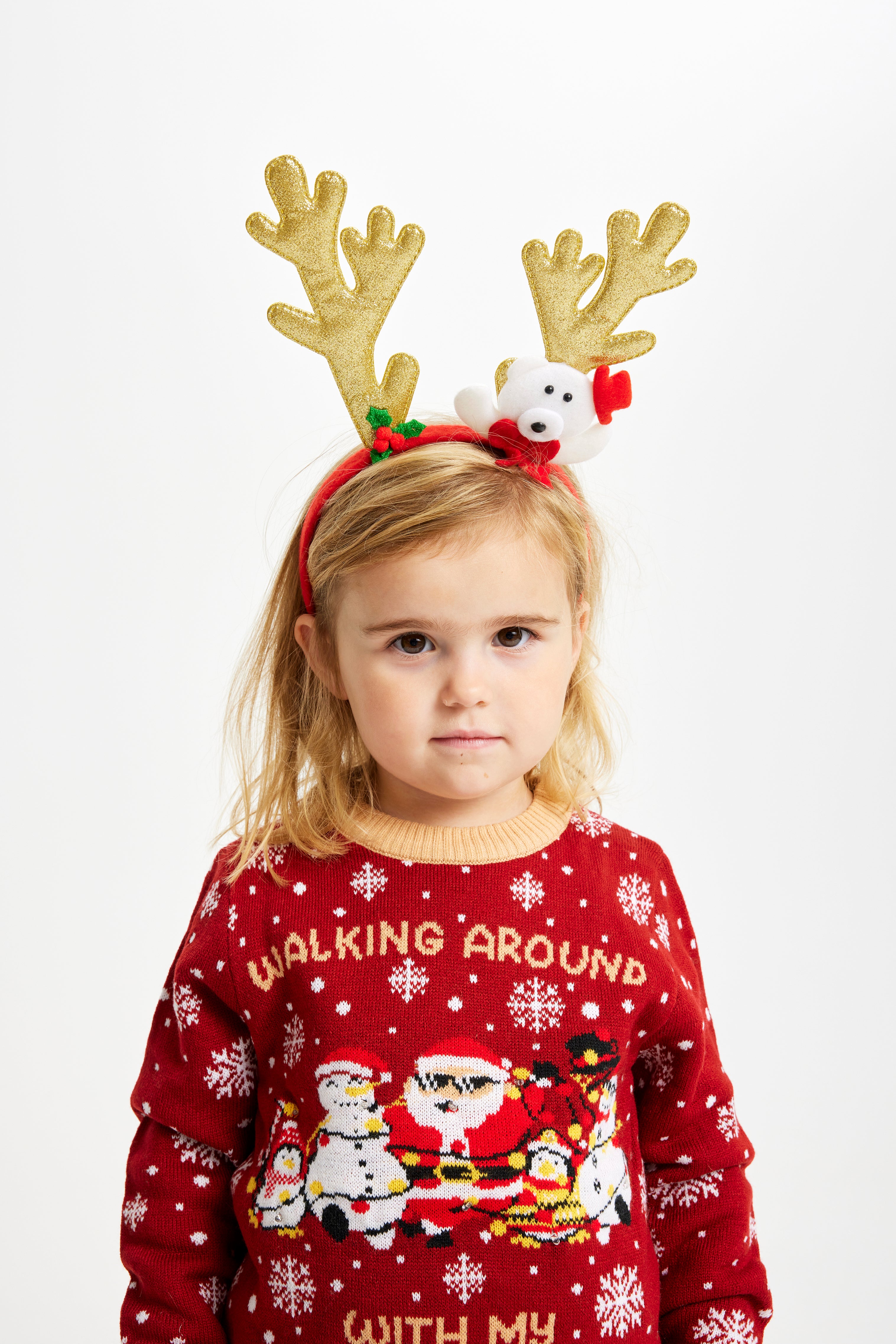 Et barn med guldfarvet rensdyrgevir er iført en rød julesweater.